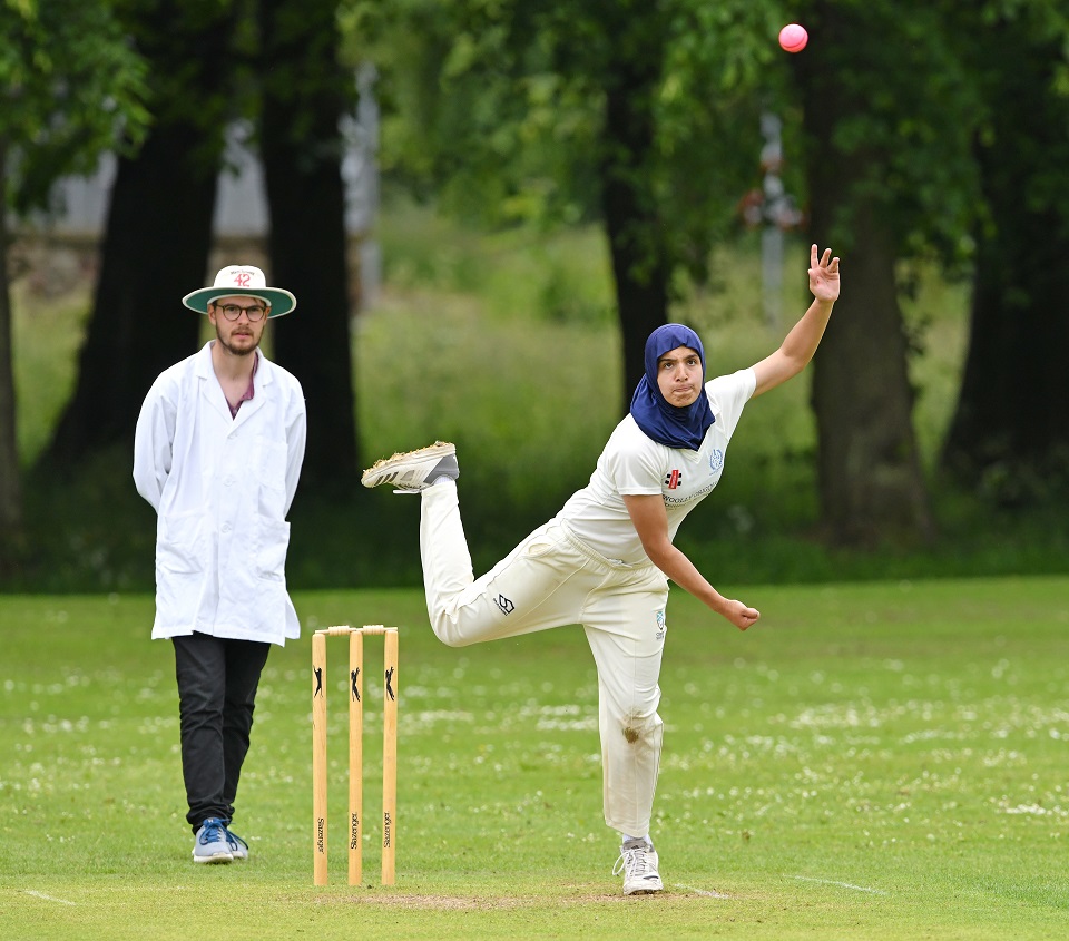 Woman bowling beside umpire in club cricket match