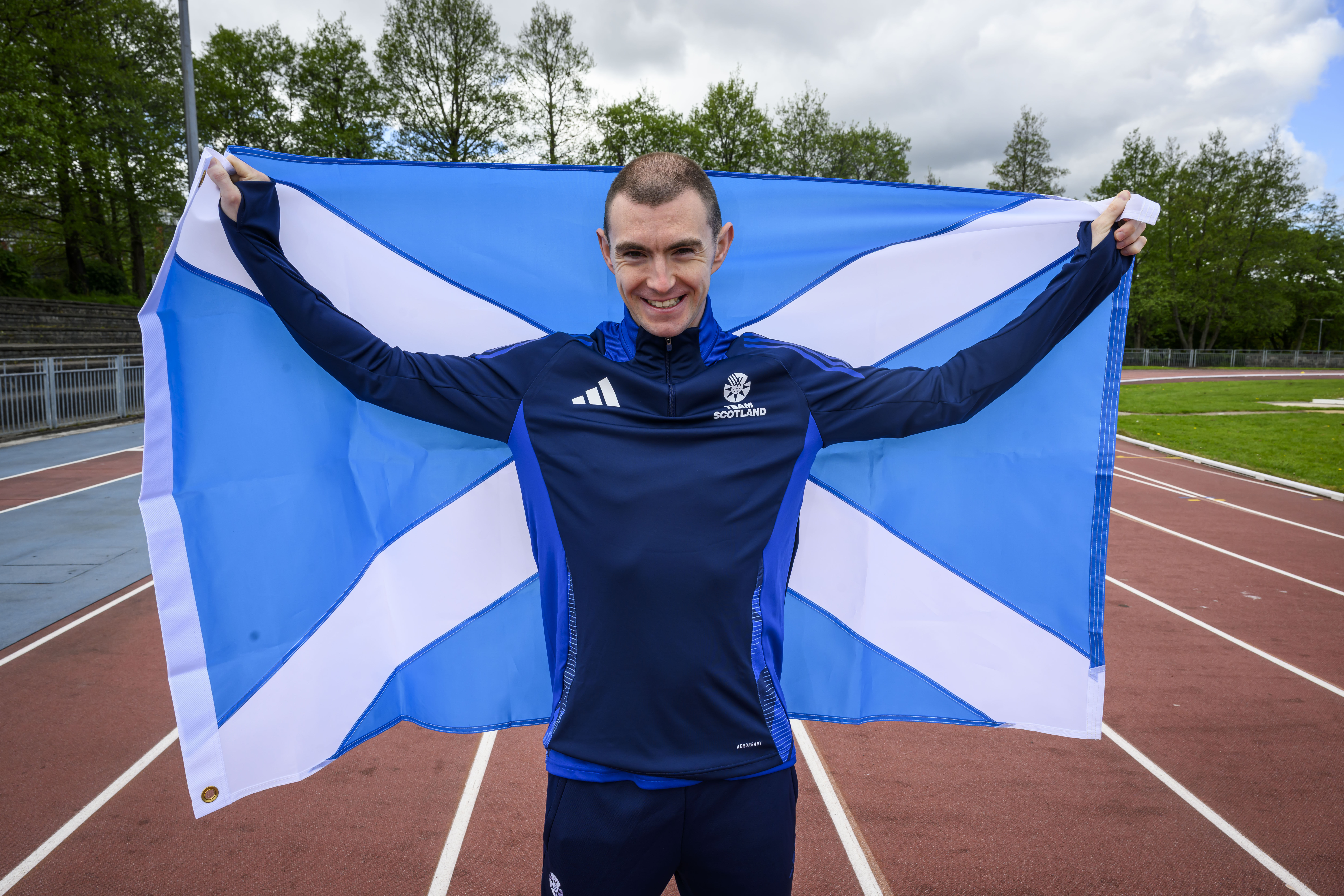Steven Bryce holding the Scottish flag on an athletics track